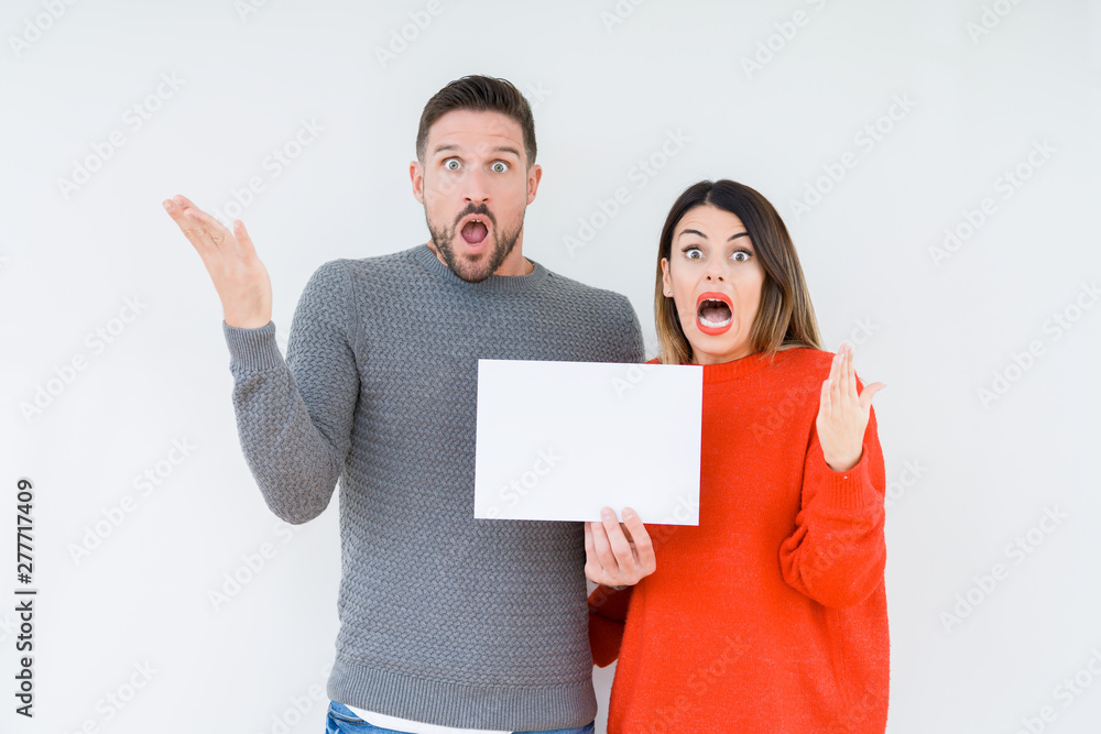 Young couple holding blank sheet paper over isolated background very happy and excited, winner expression celebrating victory screaming with big smile and raised hands Young couple holding blank sheet paper over isolated background very happy and excited, winner expression celebrating victory screaming with big smile and raised hands