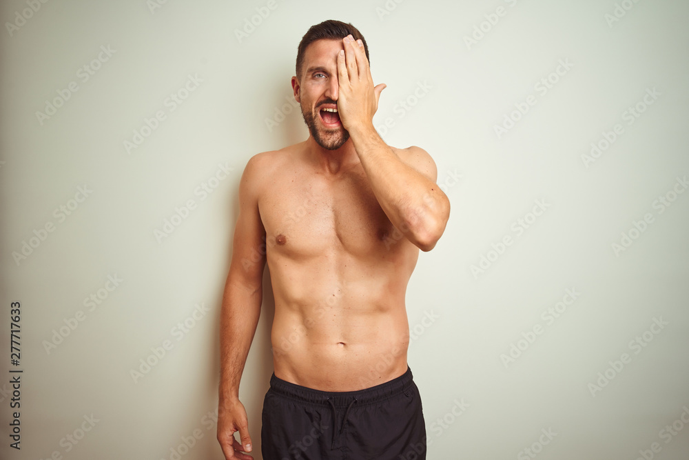 Young handsome shirtless man over isolated background covering one eye with hand, confident smile on face and surprise emotion.