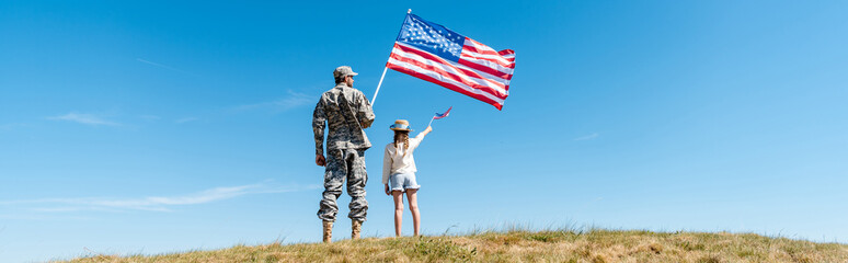 Panoramic shot of kid and military father holding American flags