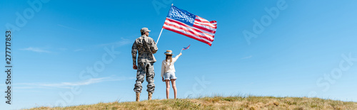 Panoramic shot of kid and military father holding American flags
