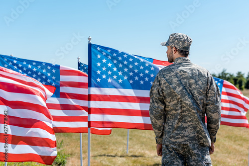 man in military uniform and cap standing near american flags