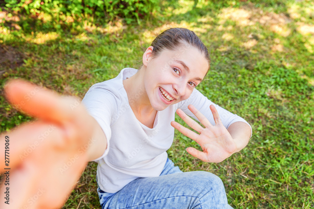 Young funny girl take selfie from hands with phone sitting on green grass park or garden background. Portrait of young attractive woman making selfie photo on smartphone in summer day Young funny girl take selfie from hands with phone sitting on green grass park or garden background. Portrait of young attractive woman making selfie photo on smartphone in summer day