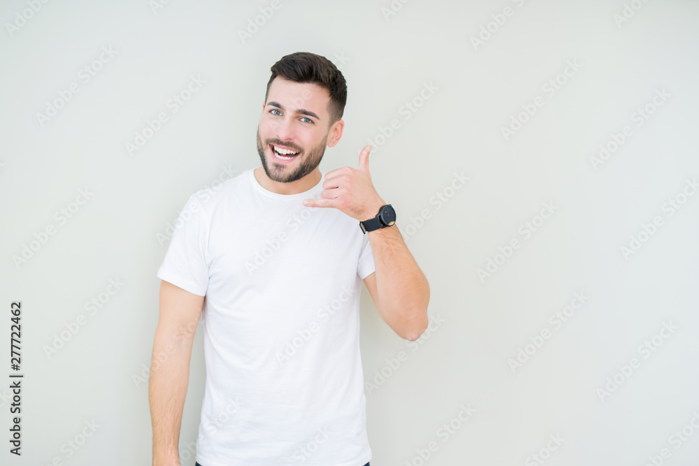 Young handsome man wearing casual white t-shirt over isolated background smiling doing phone gesture with hand and fingers like talking on the telephone. Communicating concepts. Young handsome man wearing casual white t-shirt over isolated background smiling doing phone gesture with hand and fingers like talking on the telephone. Communicating concepts.