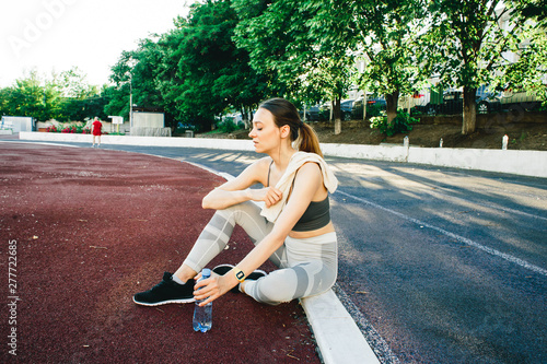pretty woman sitting on the ground with a bottle of water after Jogging outdoors © Дарья Фомина