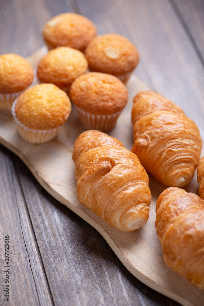 Cupcakes and croissants fresh out of the oven on wooden board. Vertical breakfast shoot. Cupcakes and croissants fresh out of the oven on wooden board. Vertical breakfast shoot.