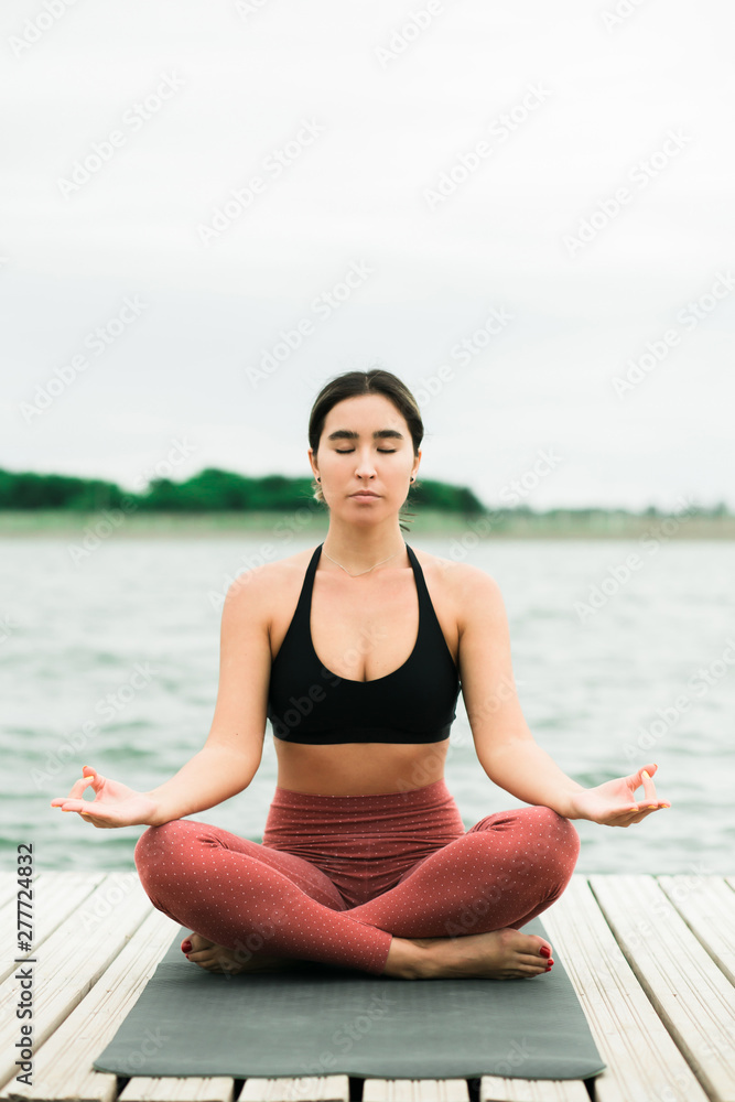 Fototapeta premium Asian young girl meditating outdoors on the pier by the lake.