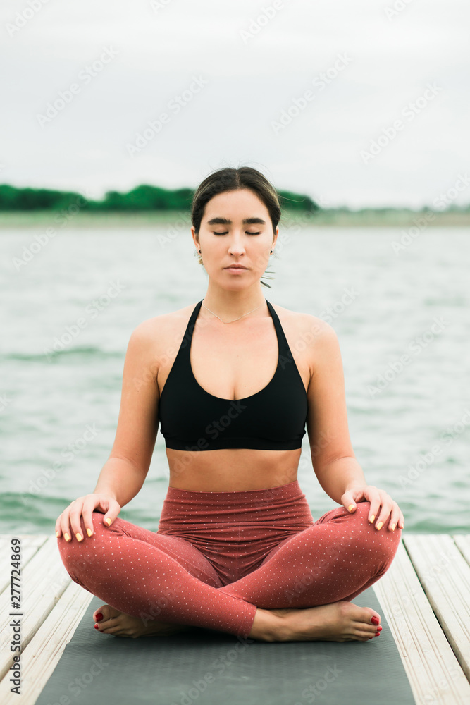 Asian young girl meditating outdoors on the pier by the lake.