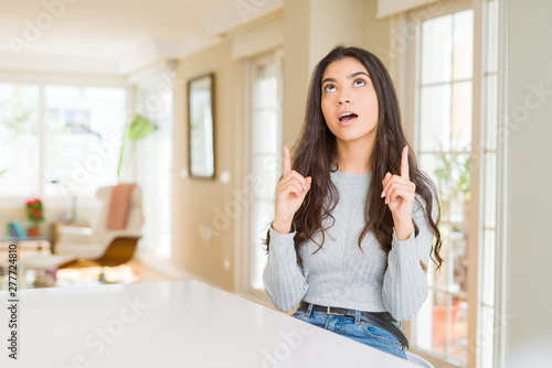 Free Download Young beautiful woman at home amazed and surprised looking up and pointing with fingers and raised arms. - GFXLoad