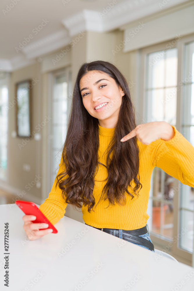 Young woman using red smartphone sending a message with surprise face pointing finger to himself Young woman using red smartphone sending a message with surprise face pointing finger to himself