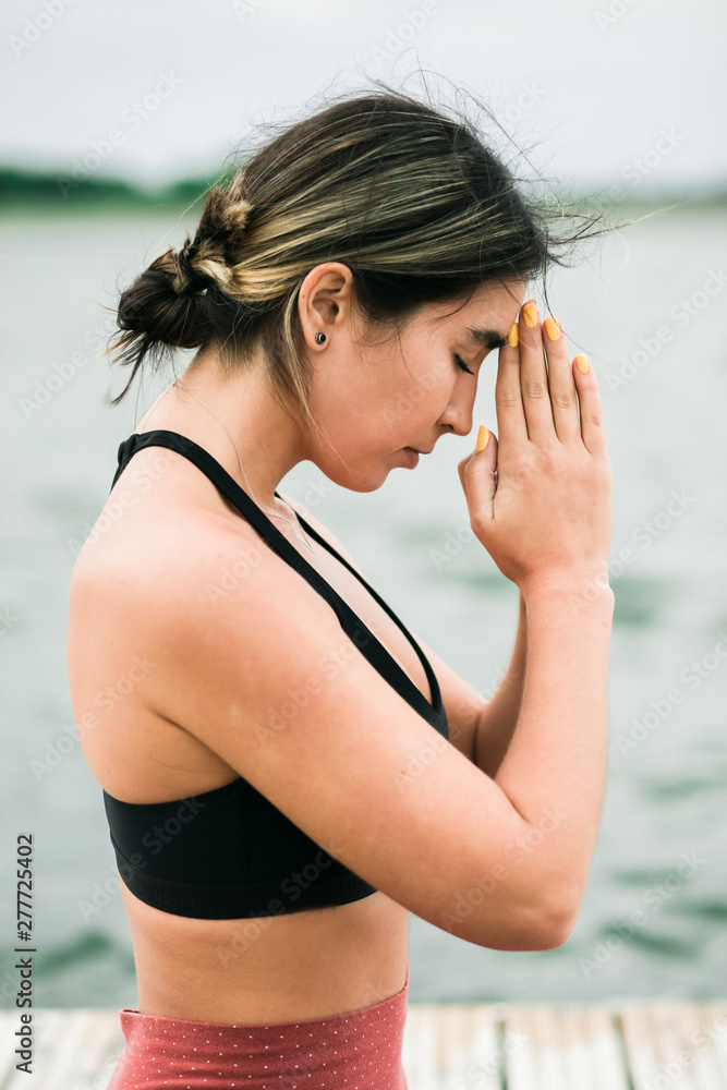 Asian young girl meditating outdoors on the pier by the lake.