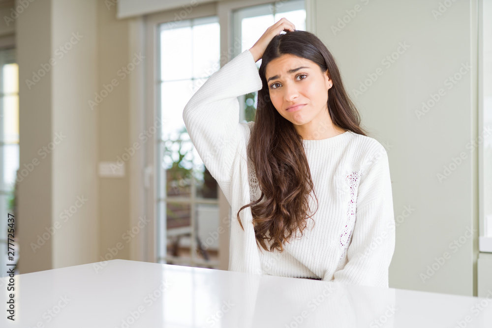 Young beautiful woman at home on white table confuse and wonder about question. Uncertain with doubt, thinking with hand on head. Pensive concept. Young beautiful woman at home on white table confuse and wonder about question. Uncertain with doubt, thinking with hand on head. Pensive concept.