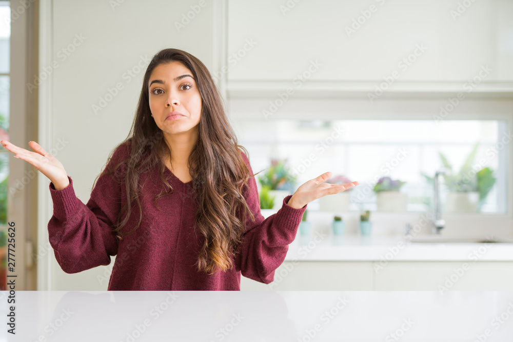 Young beautiful woman at home clueless and confused expression with arms and hands raised. Doubt concept.