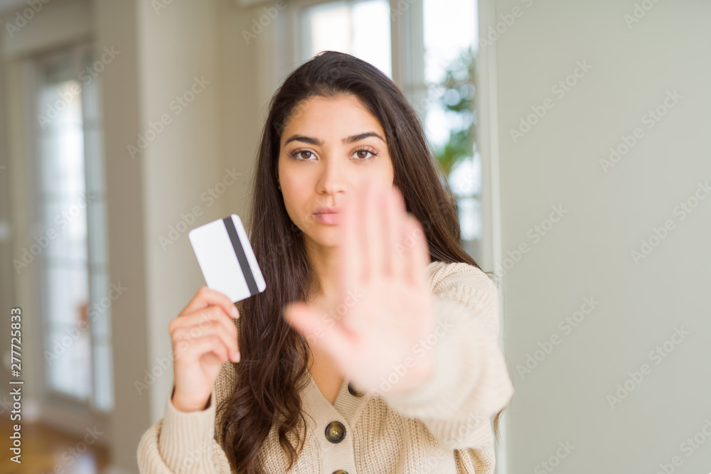 Young woman holding credit card as payment with open hand doing stop sign with serious and confident expression, defense gesture Young woman holding credit card as payment with open hand doing stop sign with serious and confident expression, defense gesture