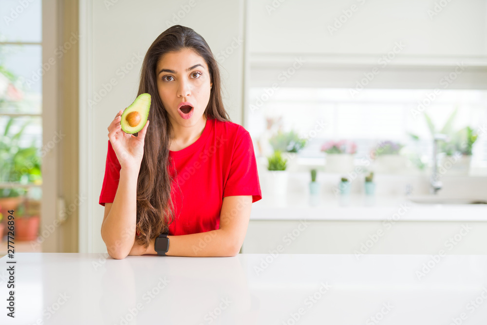 Young woman eating healthy avocado scared in shock with a surprise face, afraid and excited with fear expression Young woman eating healthy avocado scared in shock with a surprise face, afraid and excited with fear expression