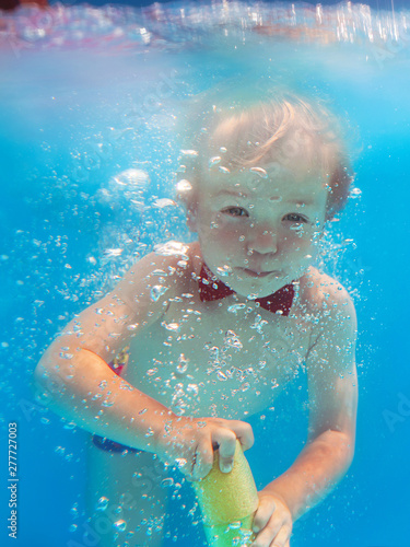 Little funny cheerful child boy with red butterfly and with water gun diving underwater in swimming pool, learn to swim. Sport and vacation concept