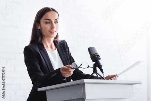 Bilde på lerret beautiful, positive lecturer holding glasses while standing on podium tribune