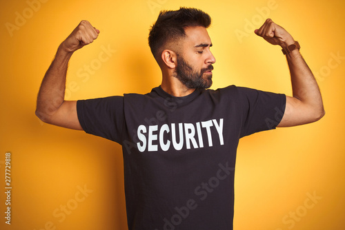 Arab indian hispanic safeguard man wearing security uniform over isolated yellow background showing arms muscles smiling proud. Fitness concept.