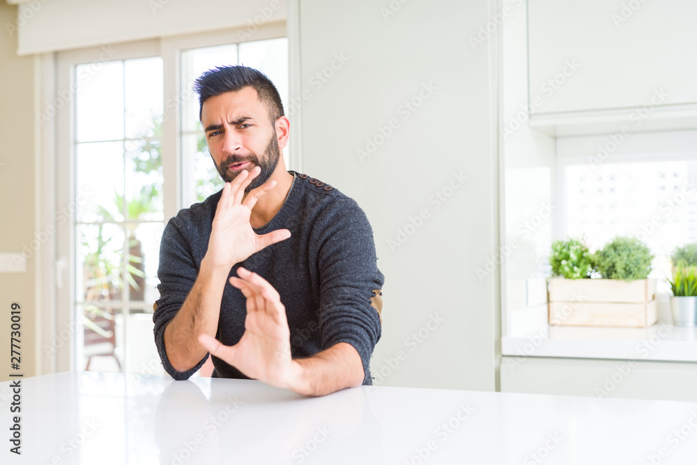 Handsome hispanic man wearing casual sweater at home disgusted expression, displeased and fearful doing disgust face because aversion reaction. With hands raised. Annoying concept.