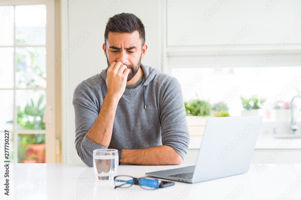 Handsome hispanic man working using computer laptop looking stressed and nervous with hands on mouth biting nails. Anxiety problem. Handsome hispanic man working using computer laptop looking stressed and nervous with hands on mouth biting nails. Anxiety problem.
