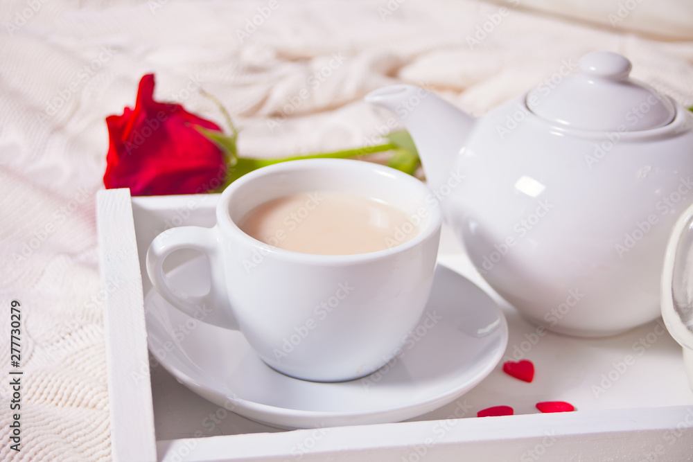 Close up of cup of tea with red roses on the white tray Close up of cup of tea with red roses on the white tray