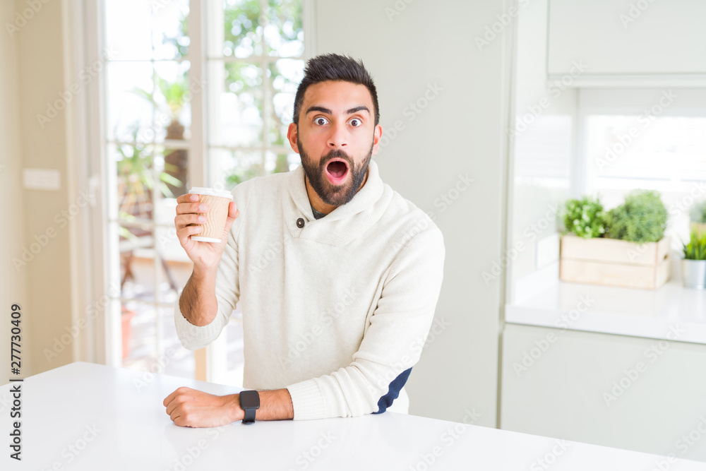 Handsome hispanic man drinking a coffee in a paper cup scared in shock with a surprise face, afraid and excited with fear expression Handsome hispanic man drinking a coffee in a paper cup scared in shock with a surprise face, afraid and excited with fear expression