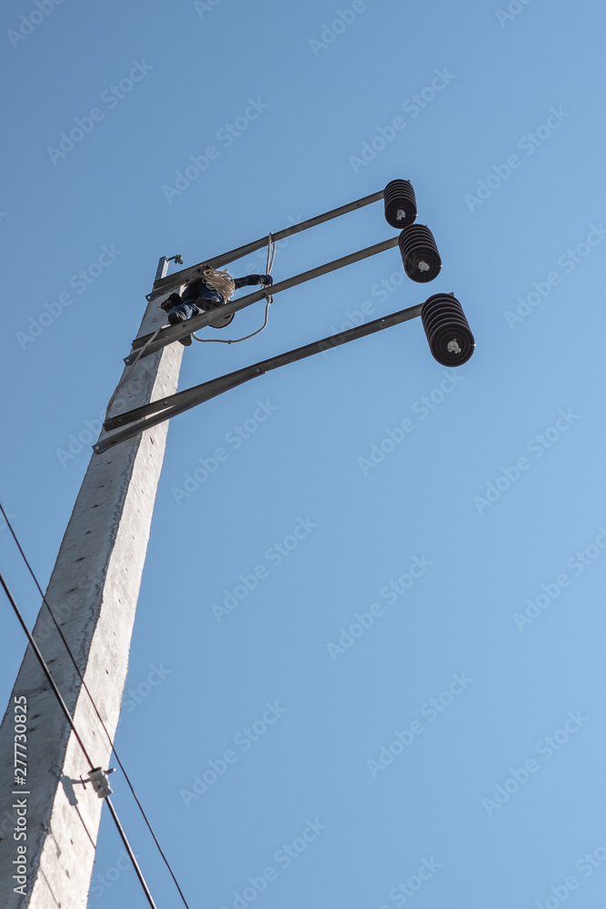 Electrician climbing very high electric power pole with safety belt to install new wire in very hot day with blue sky. Electrician climbing very high electric power pole with safety belt to install new wire in very hot day with blue sky.