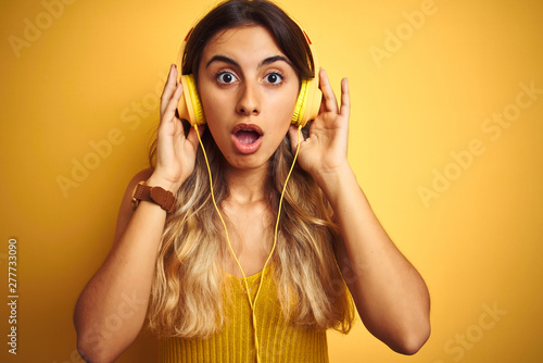Young beautiful woman wearing headphones over yellow isolated background scared in shock with a surprise face, afraid and excited with fear expression