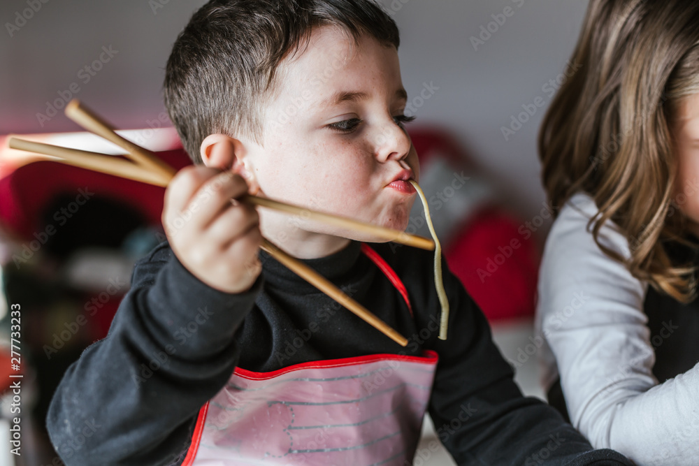 Boy °eating tasty noodles ° while sitting at table at home Boy °eating tasty noodles ° while sitting at table at home