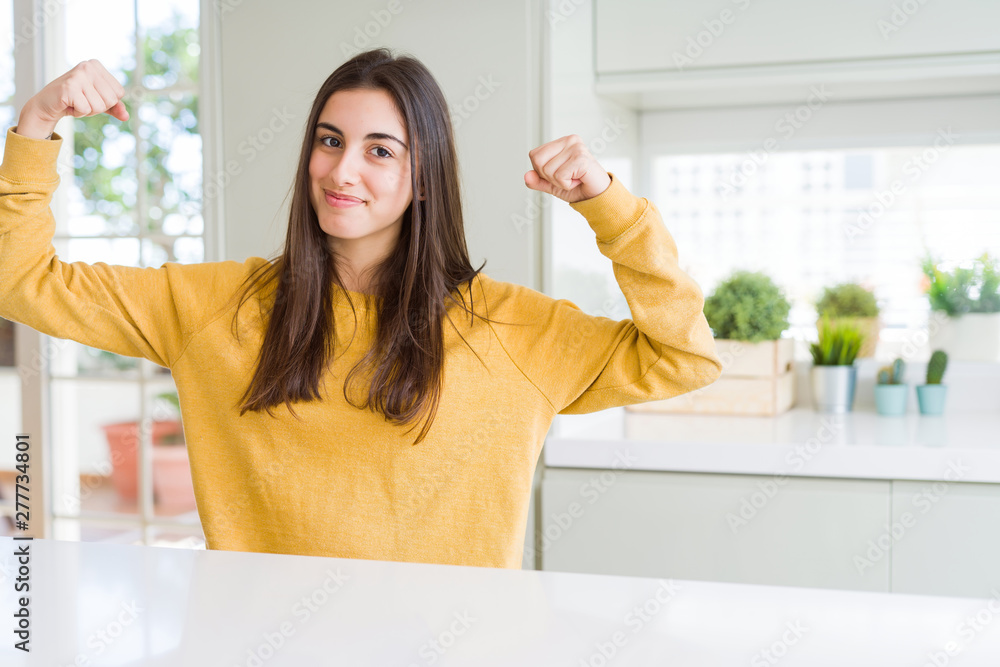 Beautiful young woman wearing yellow sweater showing arms muscles smiling proud. Fitness concept. Beautiful young woman wearing yellow sweater showing arms muscles smiling proud. Fitness concept.