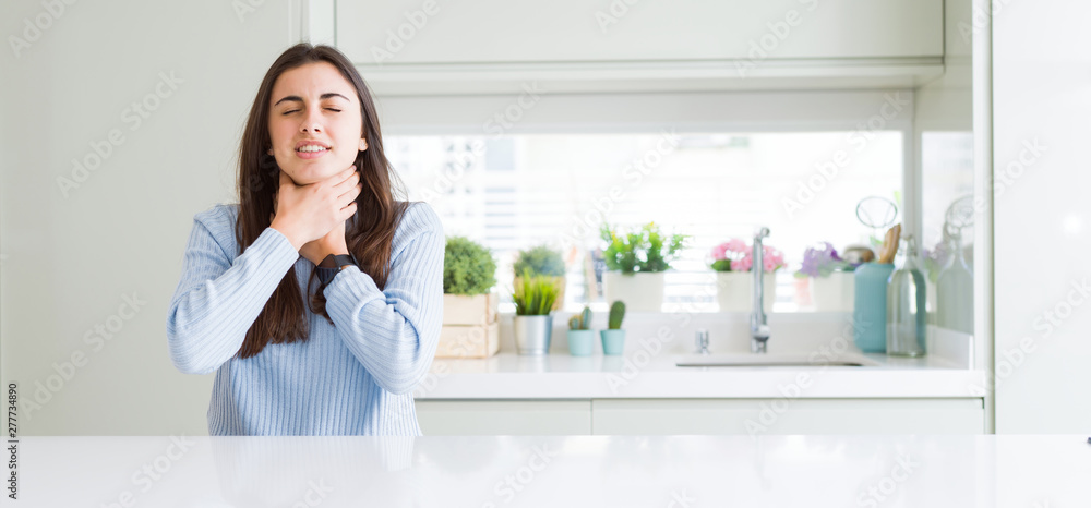 Wide angle picture of beautiful young woman sitting on white table at home shouting and suffocate because painful strangle. Health problem. Asphyxiate and suicide concept. Wide angle picture of beautiful young woman sitting on white table at home shouting and suffocate because painful strangle. Health problem. Asphyxiate and suicide concept.