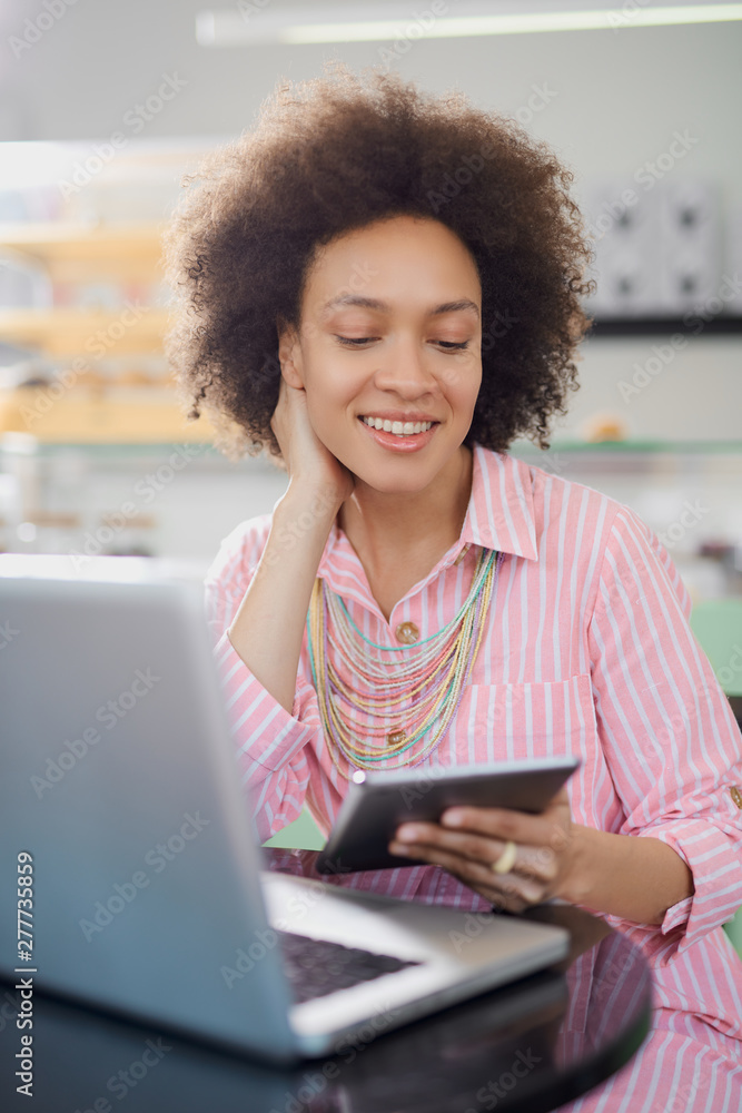 Attractive mixed race woman in striped pink dress sitting in cafe and using tablet. Attractive mixed race woman in striped pink dress sitting in cafe and using tablet.