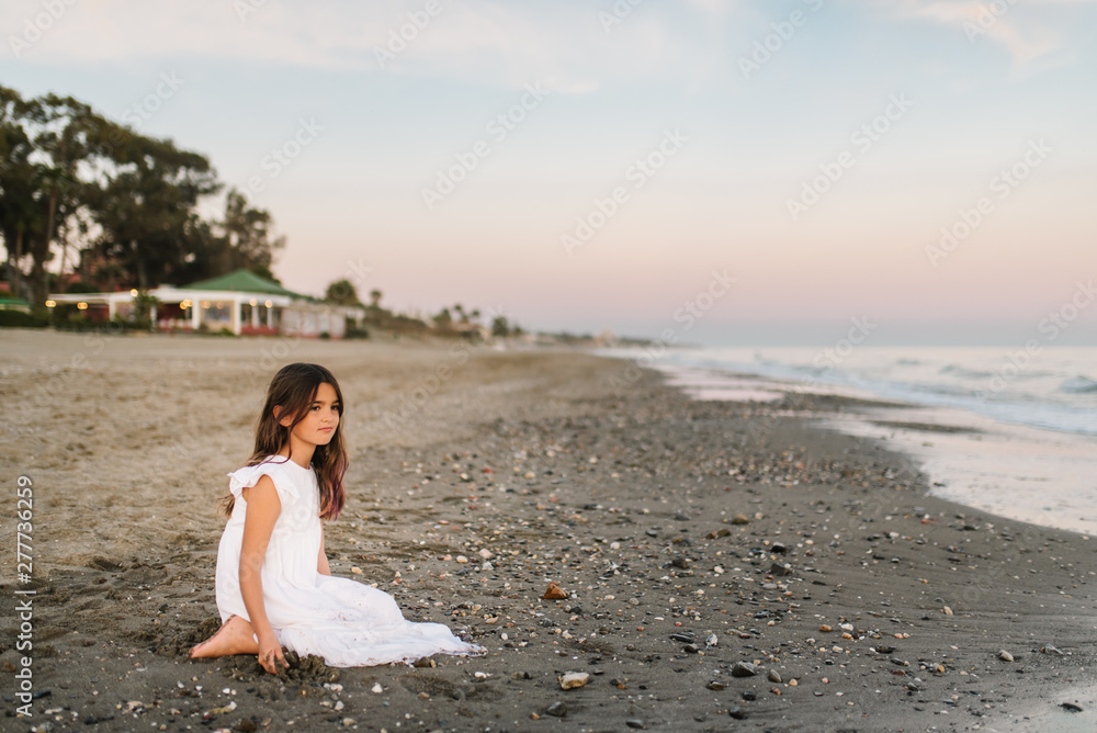 cute female child in white dress sitting on sandy seashore cute female child in white dress sitting on sandy seashore