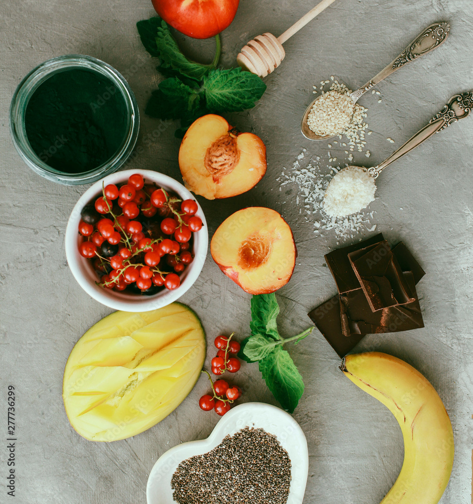 Superfoods and healthy food on a gray background with copy space Fruits: mango, banana, currant, peaches lie next to chia and spirulina seeds Top view Copy space Selective focus