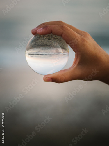 crop view of little female child with brown hair holding glass ball on background of waves photo