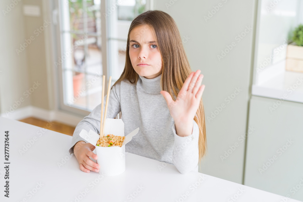 Beautiful young girl kid eating asian rice in delivery box with open hand doing stop sign with serious and confident expression, defense gesture