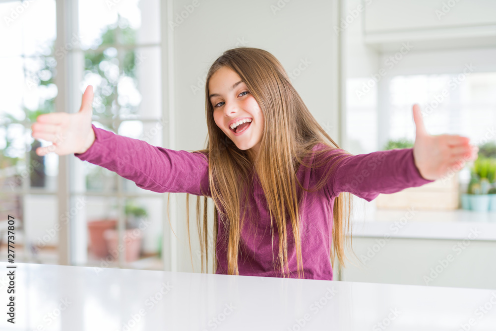 Beautiful young girl kid on white table looking at the camera smiling with open arms for hug. Cheerful expression embracing happiness. Beautiful young girl kid on white table looking at the camera smiling with open arms for hug. Cheerful expression embracing happiness.