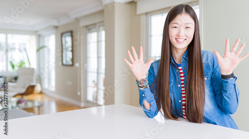 Young beautiful asian woman with long hair wearing denim jacket showing and pointing up with fingers number ten while smiling confident and happy.