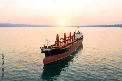 Aerial view of high-speed sea vessel for transportation of a cargo vessel at high speed is drifting near the seaport of the city at sunset. Ship on the background of blue sea water. Import, export