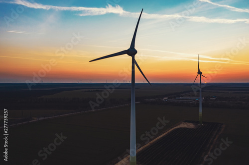 The movement of wind turbines blades in the field against the backdrop of a bright orange sunset wind park. Silhouettes of windmills with a bird's-eye view. Alternative energy sources. Drone, slide up