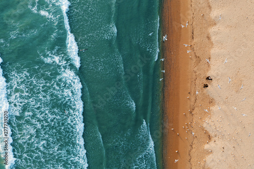 Scenic aerial view of golden sand waves and turquoise sea water with white foam from small waves. The concept of summer holidays. Bright abstract background perfect for any design