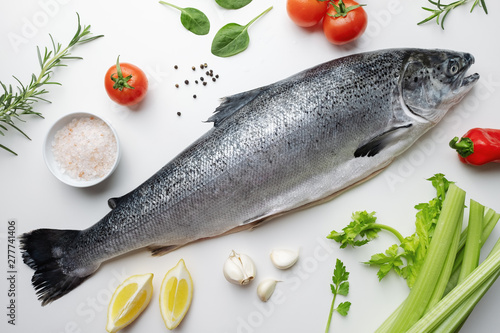 Fresh salmon fish lies on a white table. Ingredients for cooking fish, rosemary, basil, cherry tomatoes, spinach leaves, celery, lemon, garlic, spices, Hawaiian salt. Sea fish with red meat. Omega B3
