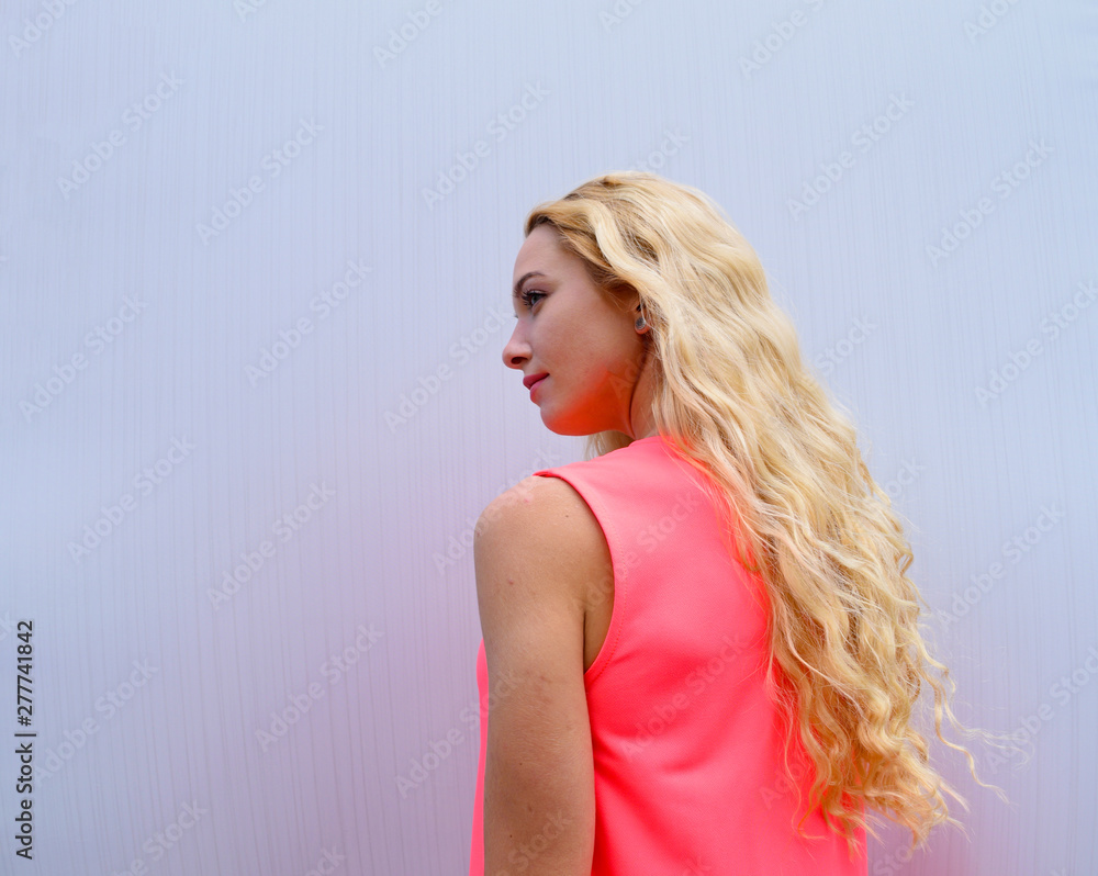 Rear view of a blonde girl in a pink dress against a white wall. Rear view of a blonde girl in a pink dress against a white wall.