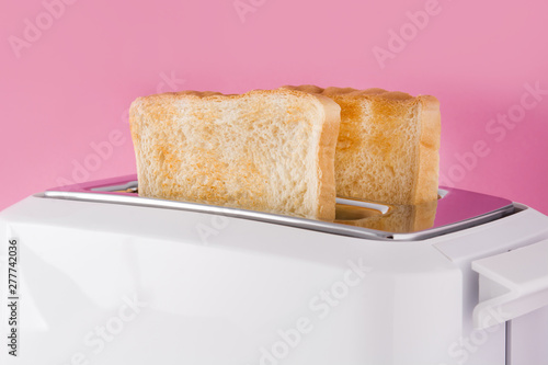 Toasted toast bread in white toaster on pink background