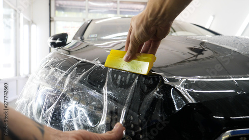Close up to PPF installation process on a front headlight and hood. PPF is a Paint Protection Film which protect paint from scratches and stone chips. Concept of: Guard, Protect, Car, New, Work.