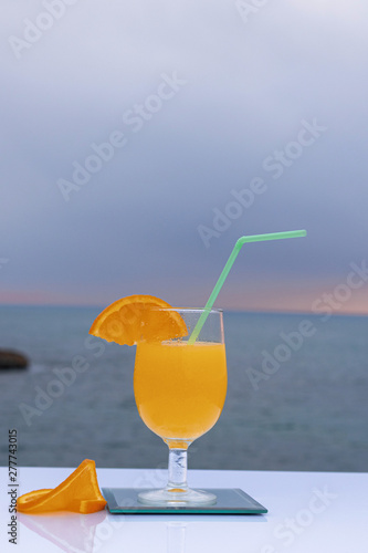 Close-up of a glass with delicious orange juice and two slices of ripe orange and the sea bottom - Fresh and ripe orange