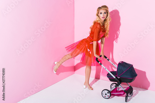 beautiful girl with baby stroller on pink with copy space, doll concept