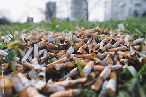 View of the pattern of scattered cigarette butts in the green grass on the meadow in the park of a big city. The problem of humanity. Smoking cigarettes, bad habit of man. Nicotine addiction. Garbage