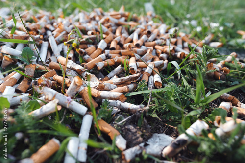 View of the pattern of scattered cigarette butts in the green grass on the meadow in the park of a big city. The problem of humanity. Smoking cigarettes, bad habit of man. Nicotine addiction. Garbage