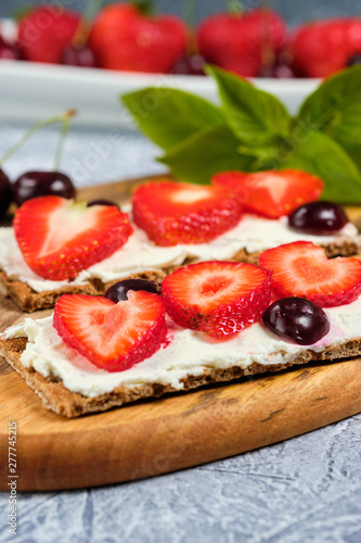 loaves with cheese  strawberries and cherries on a cutting board and gray background with mint leaves