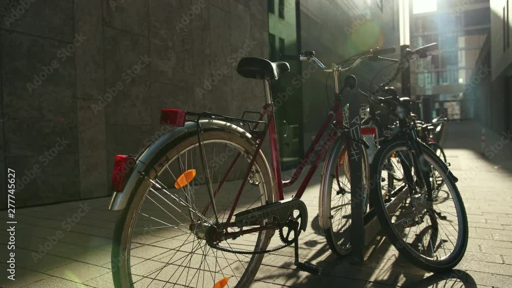 A bicycle group is parked in a cycling park. In the background is a business building. Slow and smooth hands of the camera with sun rays. Prores, close up A bicycle group is parked in a cycling park. In the background is a business building. Slow and smooth hands of the camera with sun rays. Prores, close up